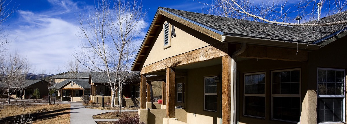 Wide view of gabled single-story homes and bare winter trees under a blue sky at La Tierra in Ruidoso