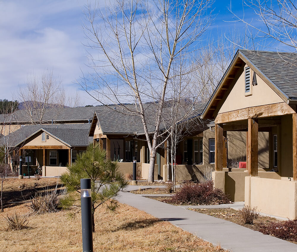 Cottage homes along a lighted central walkway with a mountain ridge behind at La Tierra in Ruidoso