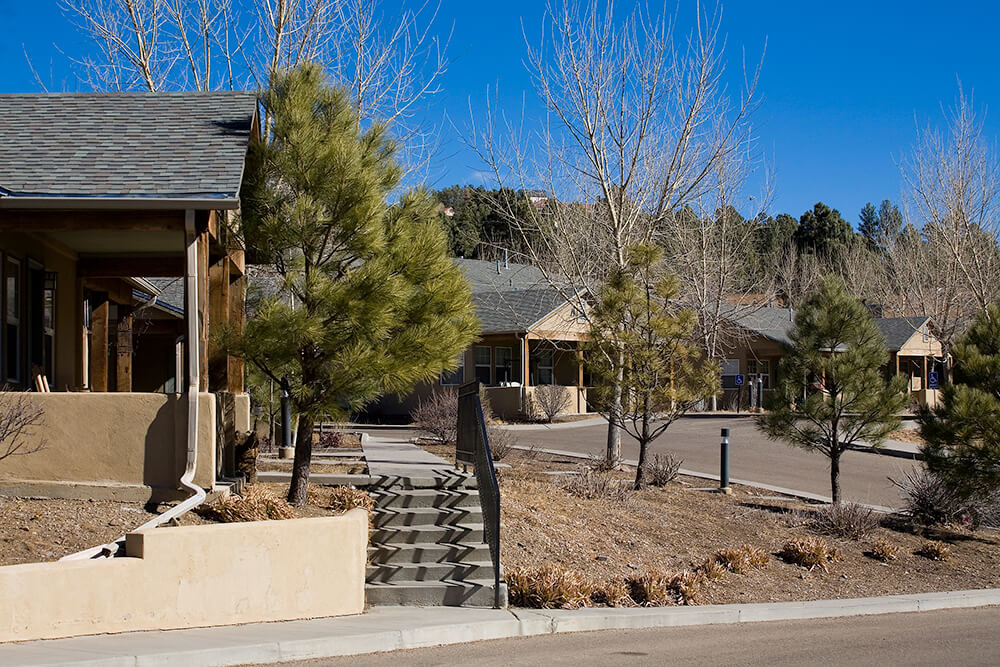Steps and landscaped grounds between single-story homes at La Tierra with a pine hillside beyond, Ruidoso NM